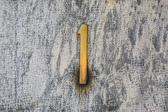 Number 1 brass house number on speckled granite wall, polished metal digit with stain marks, address sign detail for real estate, architecture and street numbering concepts and design backgrounds