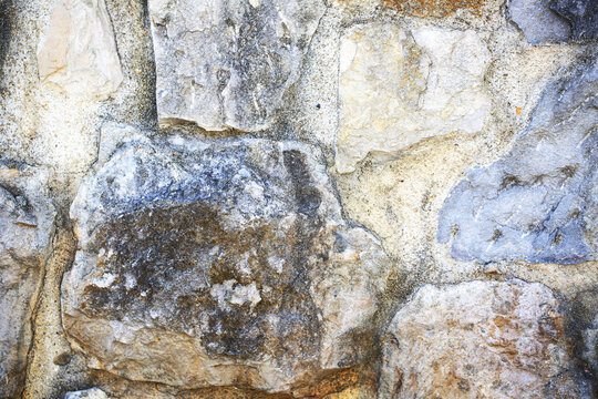 Rough natural stone wall texture with weathered rocks and cement mortar, aged masonry surface with mineral stains, old architecture background for construction, design and building material ideas
