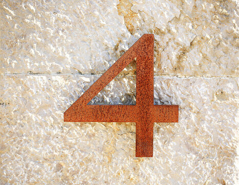 Number 4 rusty metal house number mounted on rough limestone wall, weathered corten steel digit with textured surface, architecture details for address signage, home designs and urban backgrounds