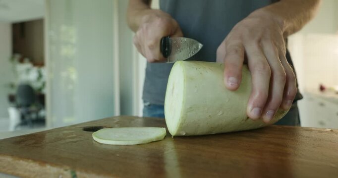 Close-up male hands cut zucchini with knife on wooden cutting board. 4K 10-bit