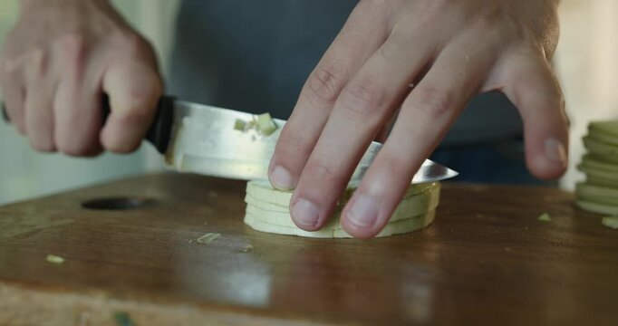 Close-up male hands cut zucchini with knife on wooden cutting board. 4K 10-bit