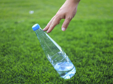 Hand reaching toward a plastic bottle on grass, with disposable beverage packaging central to litter collection and cleanup addressing plastic pollution through recycling and waste management.