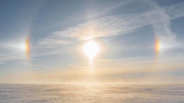 Rare symmetrical sun dog rainbow phenomenon featuring two radiant parhelia flanking the sun over a vast frozen winter landscape.
