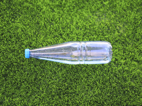 Clear plastic bottle with a blue cap lies on grass, a common form of single use beverage packaging at the center of environmental concerns about litter and the collection of recyclable plastic waste.