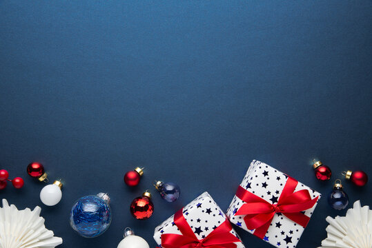 Blue Christmas and Happy New Year holiday background with gift boxes, red ribbon bows and festive red ornaments, flat lay with copy space. Greeting card.