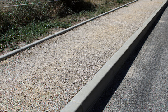 Trottoir en graviers d&eacute;limit&eacute; par des bordures en b&eacute;ton le long d'une chauss&eacute;e en enrob&eacute;