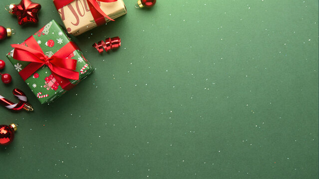 Green Christmas and Happy New Year holiday background with gift boxes, red ribbon bows and festive red ornaments, flat lay with copy space. Greeting card.
