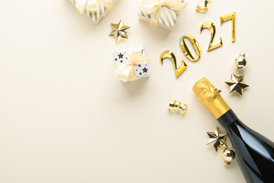 Merry Christmas and Happy Holidays greeting card, frame, banner. New Year 2027. Golden Christmas ornaments and gifts, presents with champagne on beige background top view. Space for text.