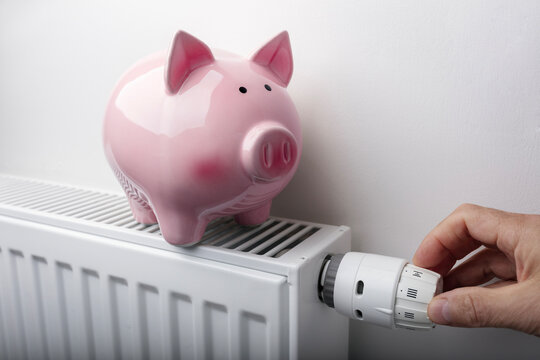 Piggy bank on top of radiator adjusting temperature on thermostat background