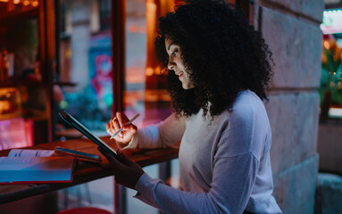 Close up profile of smiling young woman drawing with smart stylus tool on tablet computer screen in cozy evening cafe, creative freelancer or distance e-learning concept portrait © BullRun