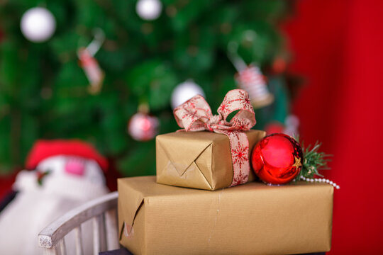 Golden Christmas Gift Boxes Wrapped with Ribbon Bow and Red Bauble on Blurred Tree Background for Holiday Celebration