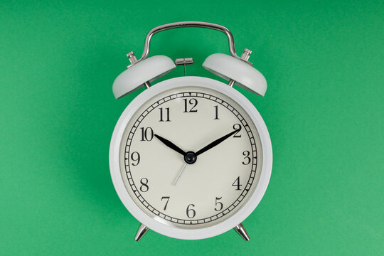Retro alarm clock on green background. White vintage twin bell alarm clock. Morning wake up and time management concept
