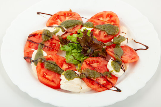 Fresh caprese salad with ripe red tomato slices, mozzarella cheese, basil pesto sauce and balsamic glaze on white plate, healthy Italian appetizer