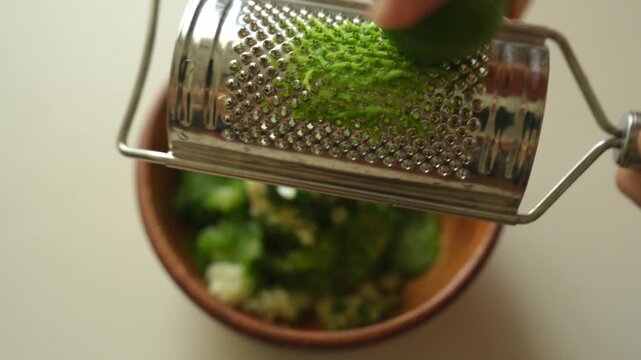 Grating lime zest over a wooden bowl of cucumber salad ingredients