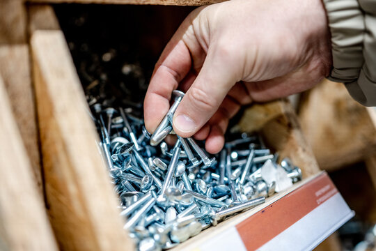 Hand selecting metal bolts from storage bin at store