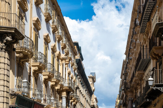Narrow street lined with historic buildings featuring classical facades and wrought-iron balconies on Via Maqueda in Palermo, Sicily, Italy