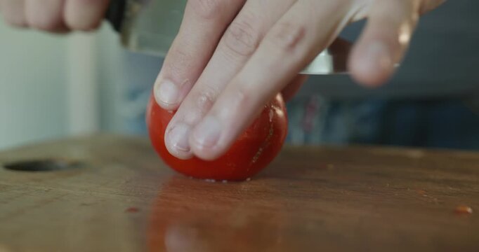 Close-up male hands cut tomato with knife on wooden cutting board. 4K 10-bit