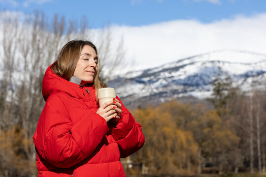 Happy woman smelling hot coffee on thermo mug with snow capped mountains behind