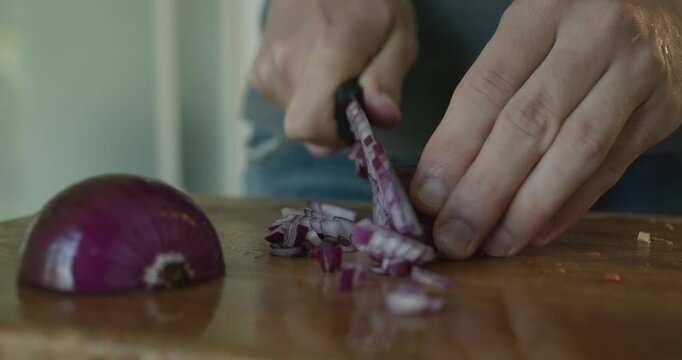 Close-up male hands cut onion with knife on wooden cutting board. 4K