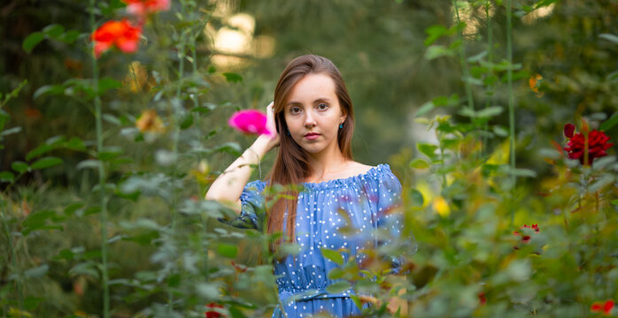 Young woman in a blue dress standing among blooming flowers in a lush garden, enjoying nature, spring atmosphere and peaceful outdoor lifestyle.