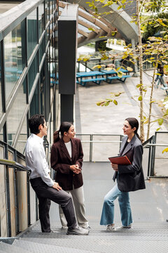 Three colleagues discuss work on an outdoor office stairway