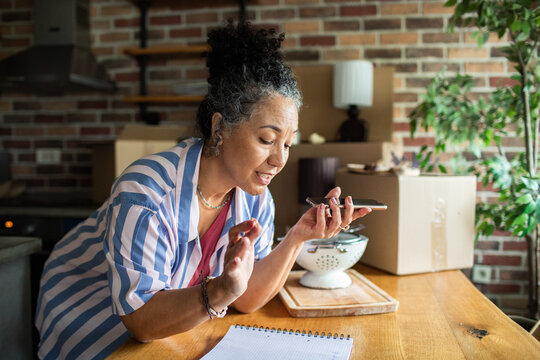 Mature woman using speakerphone while unpacking in kitchen