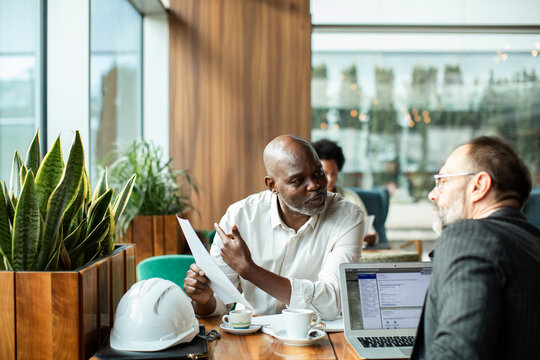 Colleagues discuss document in cafe with hard hat