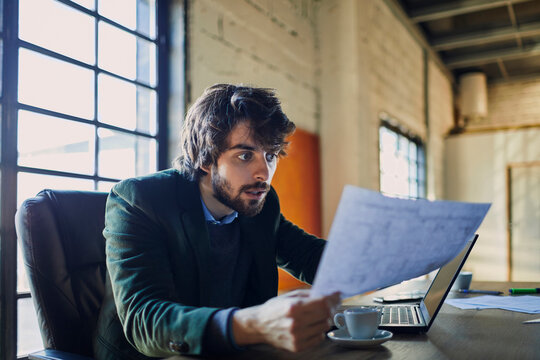 Surprised man reading document at laptop in office
