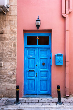 A vibrant blue wooden door set against a salmon pink wall on a charming street in the Greek islands, featuring a vintage mailbox