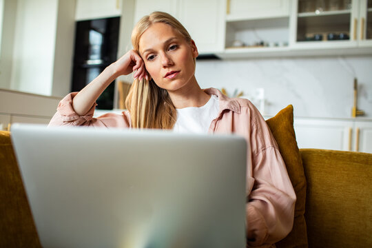 Tired woman leaning on hand while working on laptop at home