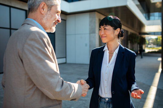 Businessman and businesswoman shaking hands outside office building