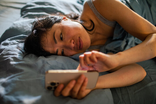 Woman scrolling smartphone while lying in bed