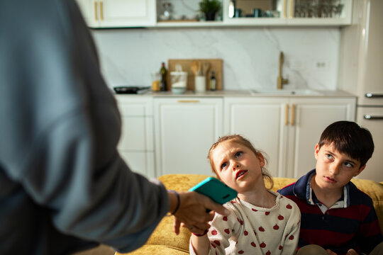 Adult taking smartphone from upset girl at home