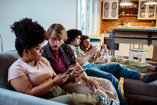 Friends lounging on a sofa using smartphones at home