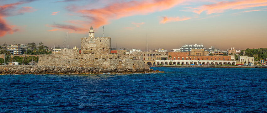 Fort of Saint Nicholas in Rhodes, Greece, guarding Mandraki Harbor with its circular stone tower, lighthouse, and medieval walls overlooking the historic harbor entrance.