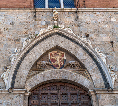 Entrance portal of Palazzo Pubblico in Siena, Italy, featuring a Gothic stone arch, lion coat of arms, and sculpted she-wolves linked to the city's legendary founders.