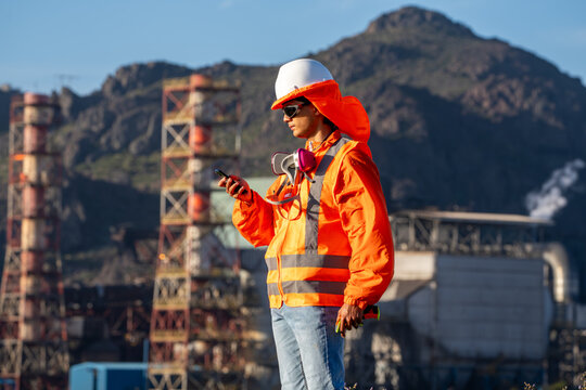 Industrial worker checking a smartphone while carrying a respirator at an outdoor mining site