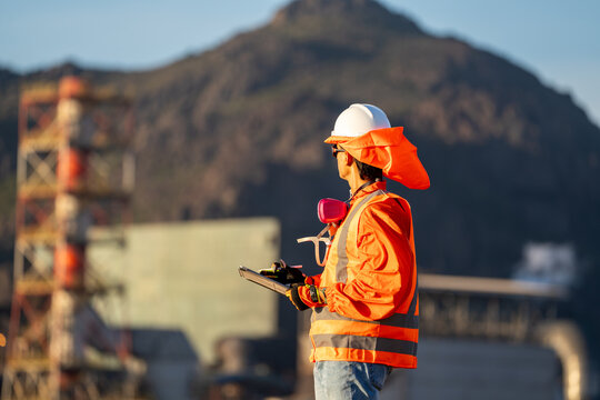 Safety inspector in protective gear monitoring an industrial site while using a tablet
