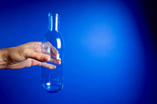 Close-up of a man's hand holding an empty glass water bottle against a vibrant blue background.