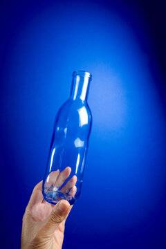 Close-up of a man's hand holding an empty glass water bottle against a vibrant blue background.