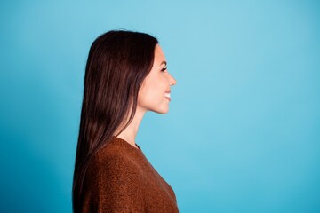 Smiling woman in profile with long dark hair against bright blue background wearing a brown sweater, casual studio portrait conveying warmth and confidence © deagreez