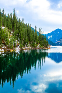 Lake Kolsai in spring. A beautiful spring mountain landscape in Kazakhstan. The blue lake is set against a backdrop of green spruce trees and still-snow-capped mountains.