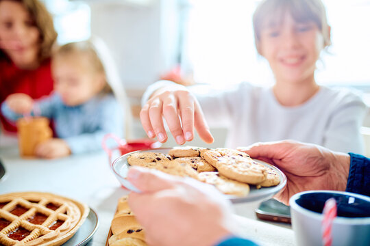 Family members sharing cookies at home, with a child reaching toward a plate of treats during a cheerful kitchen snack
