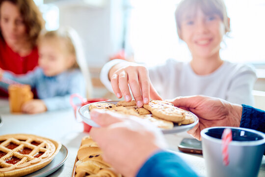 Family members sharing homemade cookies at the kitchen table, children reaching for treats during a joyful gathering