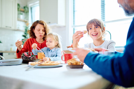 Family gathering around the kitchen table, sharing breakfast and holiday treats as children smile during a cozy Christmas morning