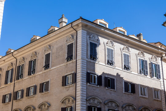 Historic corner building with ornate window pediments and dark wooden shutters against blue sky in Rome, Italy