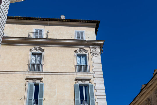 Facade of a historic ochre building with blue shutters and balconies against a deep blue sky in Rome, Italy