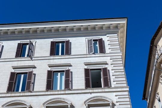 Low angle view of a neoclassical building facade with brown shutters against a deep blue sky in Rome, Italy