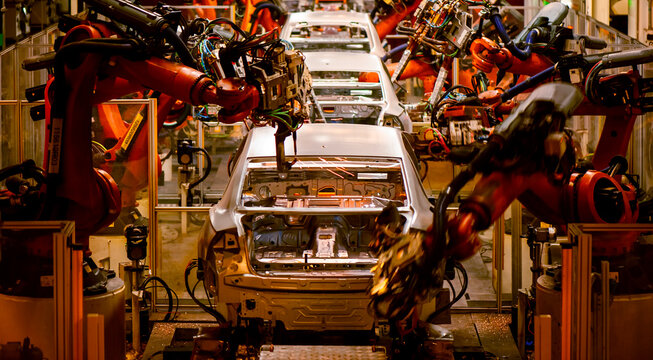 Automotive factory assembly line, industrial robotic arms spot welding car body-in-white shell, automated automobile manufacturing plant with welding sparks 