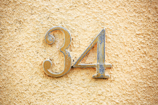 Number 34 in ornate vintage house numerals made of weathered brass mounted on rough peachy stucco wall, antique address sign, street detail, building facade, textured plaster, Mediterranean style
